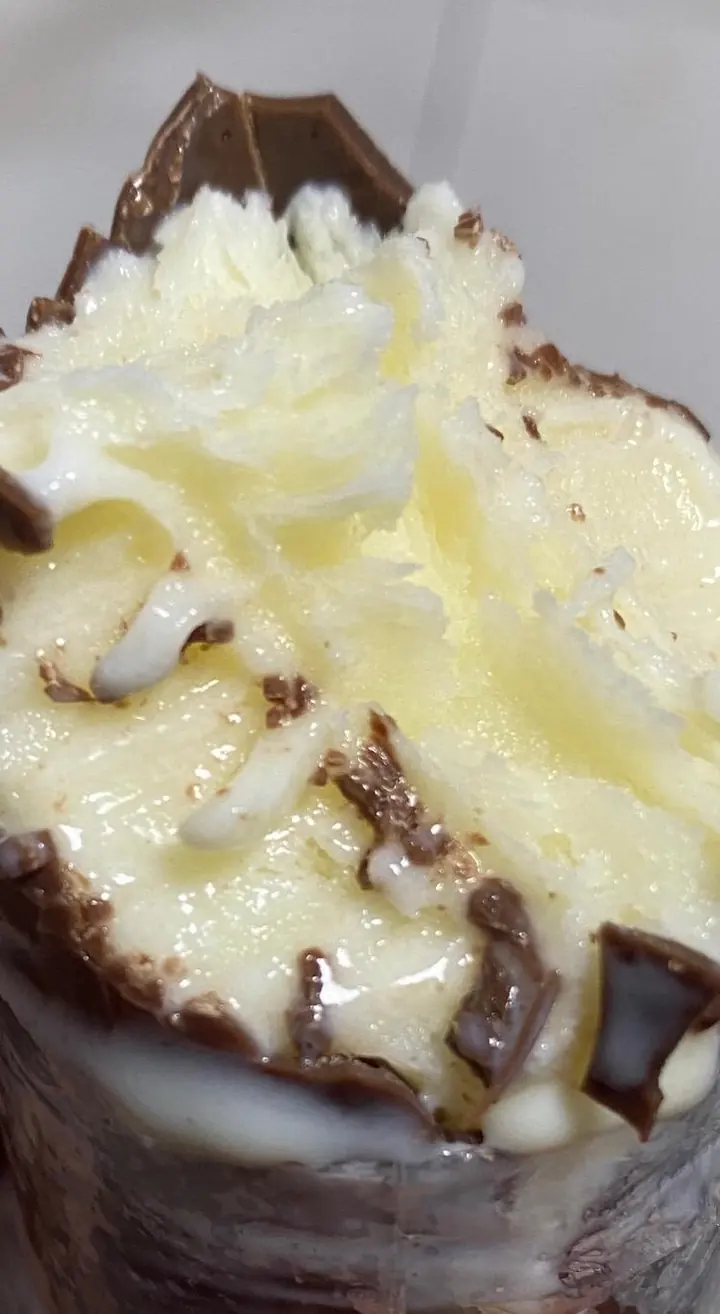 Geladinho de Ninho com casquinha de chocolate mordido, mostrando o recheio cremoso